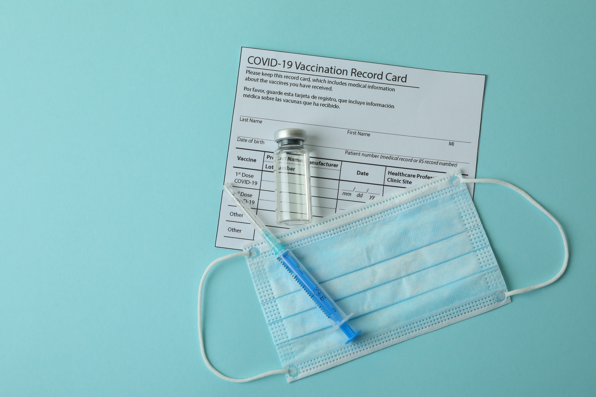 Vaccination record card, mask and syringe on blue background